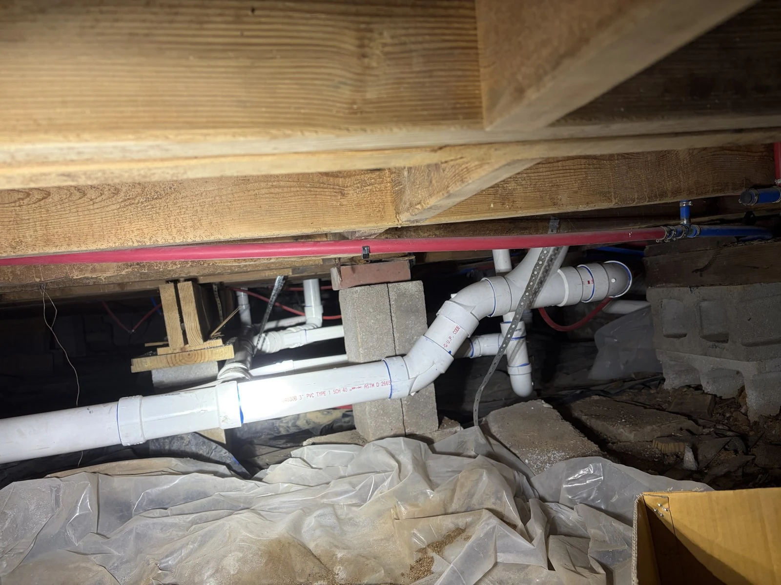 Three-inch PVC drain line with elbow fittings and couplings supported by metal straps in a Rogers, Arkansas crawlspace.