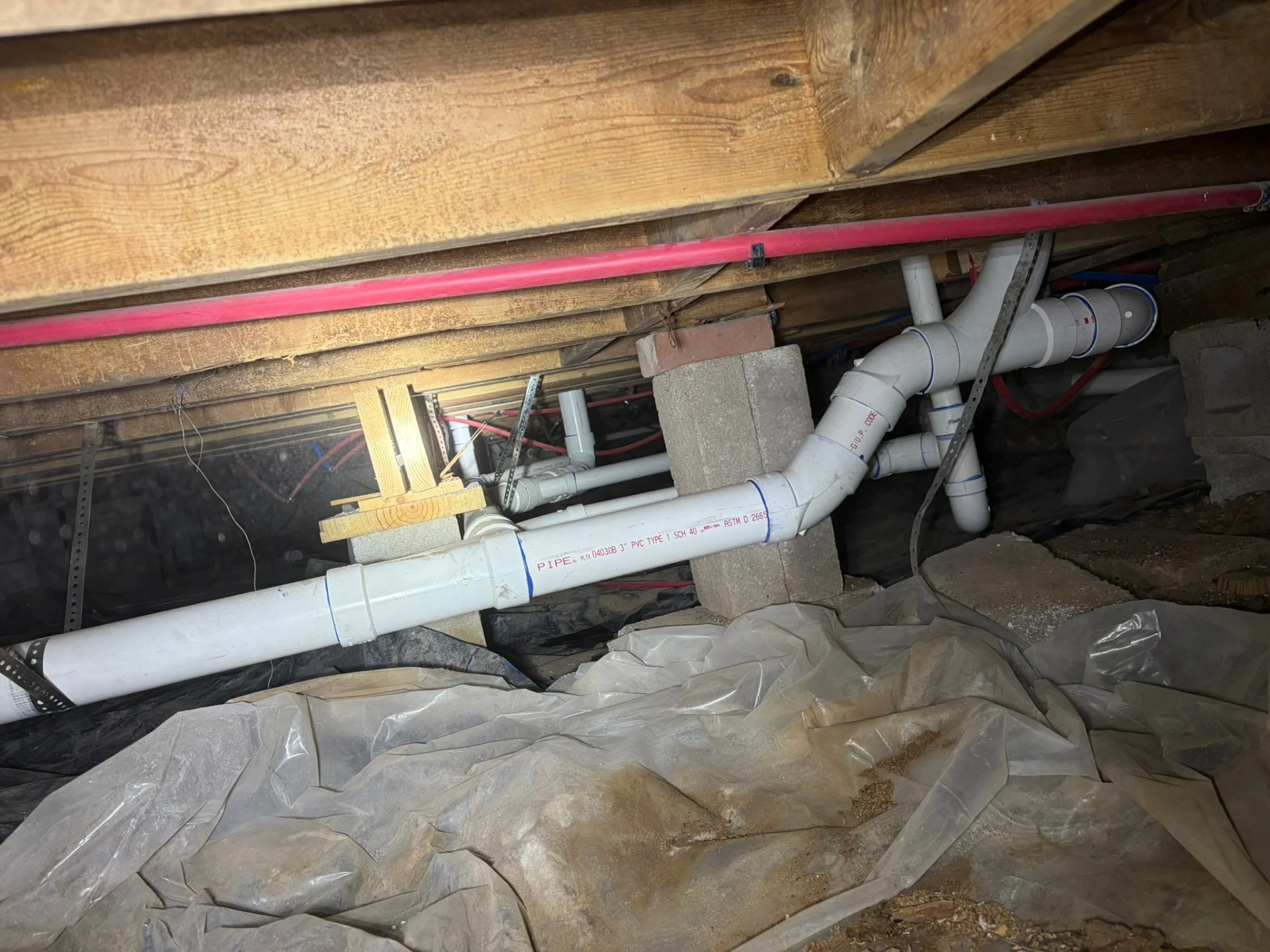 New PVC drain pipes with fittings and metal strap supports installed in a Rogers, Arkansas crawlspace.