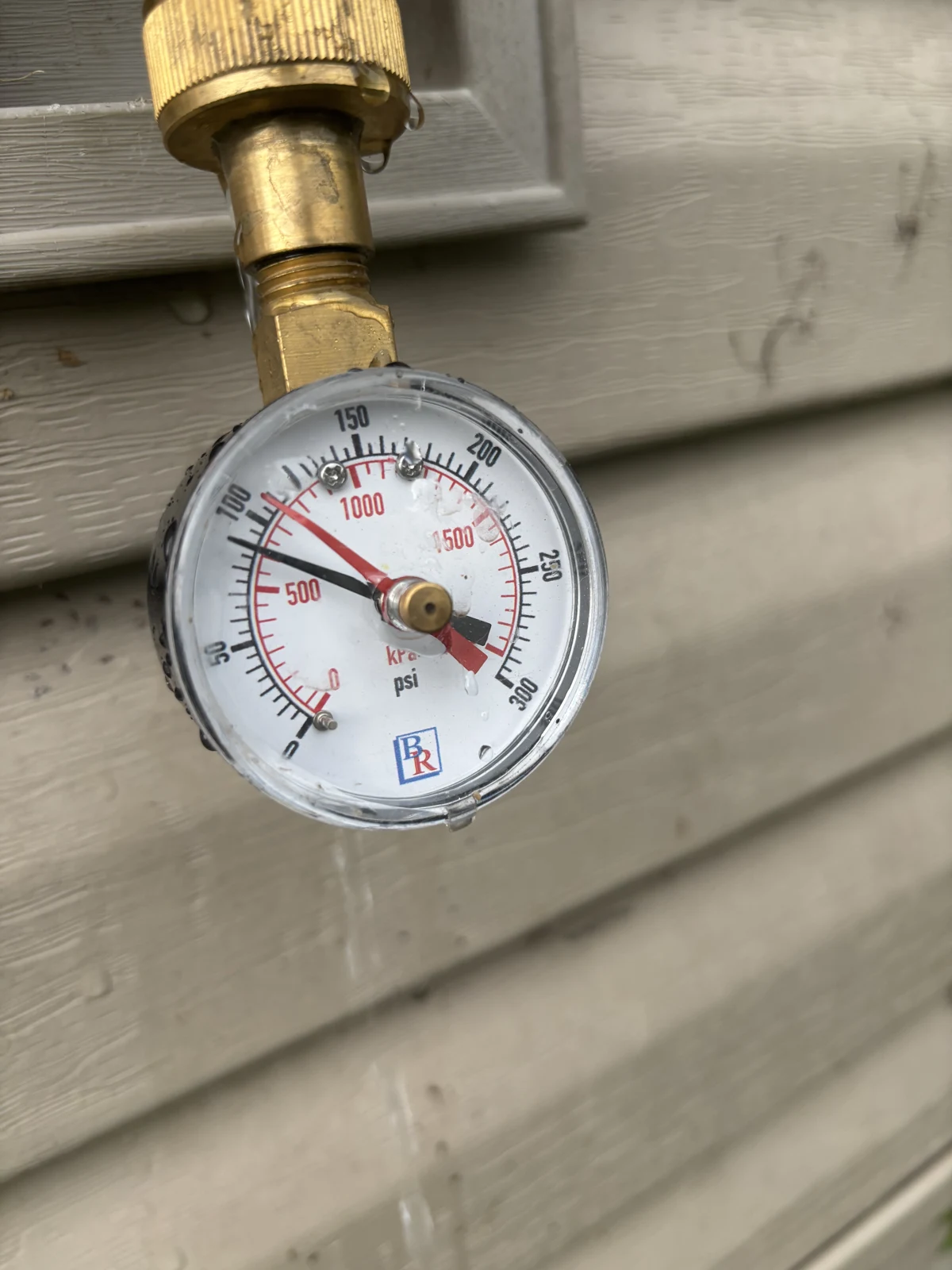 Water pressure test gauge on an outdoor hose bibb showing pressure above 80 PSI at a Fayetteville, Arkansas home.